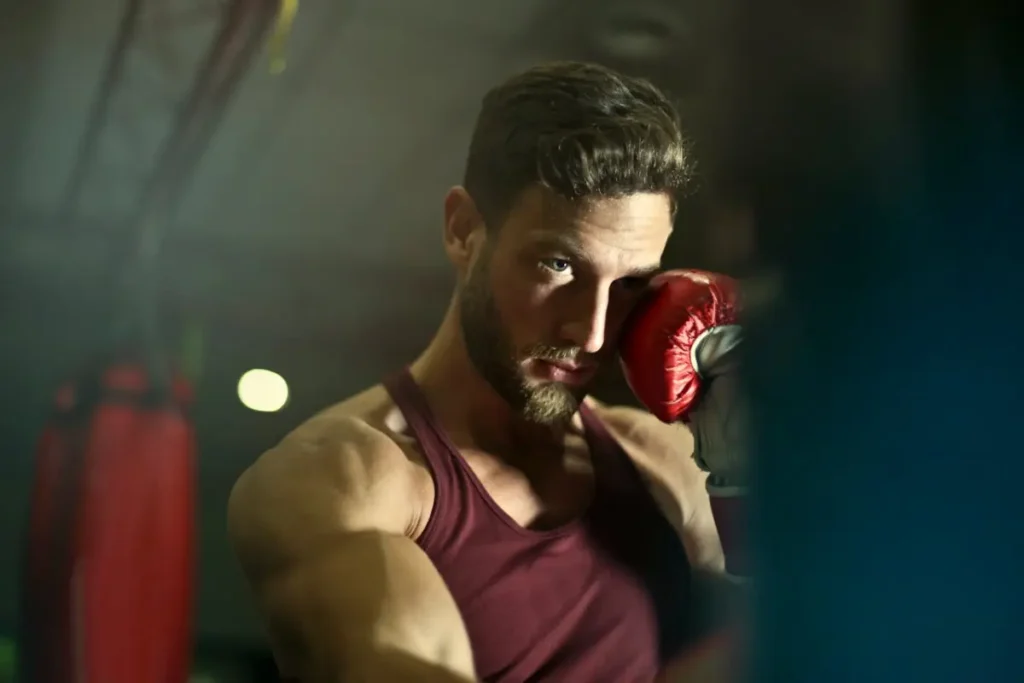 A short-bearded man in a boxing gym, holding a glove in his hand.