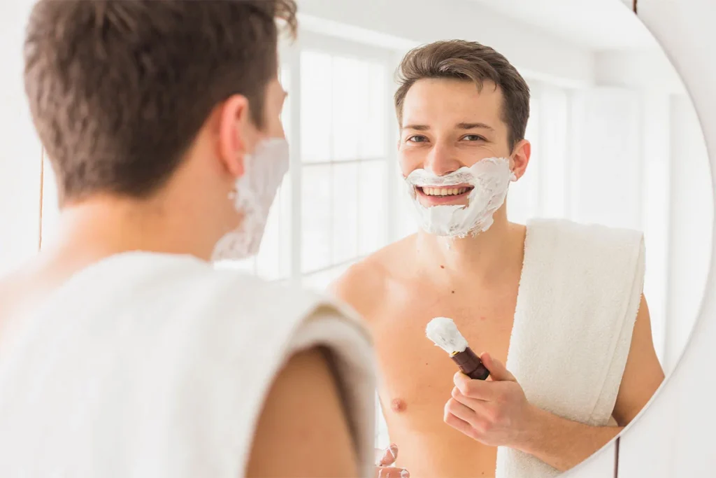 a contented man shaving in front of a mirror with a towel on his shoulder