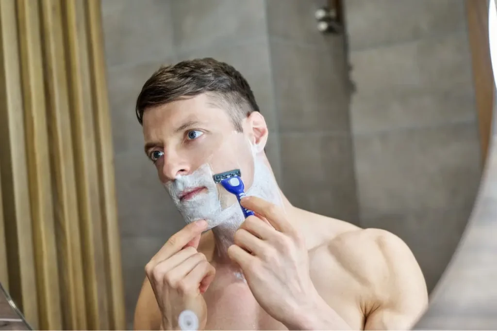 man shaving his beard in front of the mirror